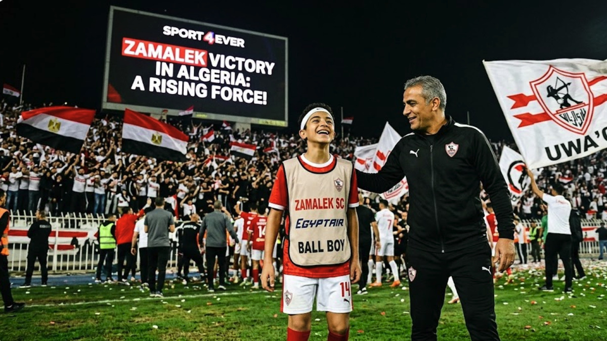 A young ball boy smiling next to a coach in a stadium with Zamalek fans celebrating in the background and a large screen showing "Zamalek Victory in Algeria".