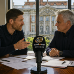 Two football managers discussing transfer market tactics inside a conference room with football documents on the table.